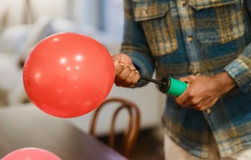 faceless ethnic guy using manual air inflator while blowing balloons at home