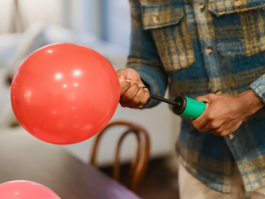 faceless ethnic guy using manual air inflator while blowing balloons at home